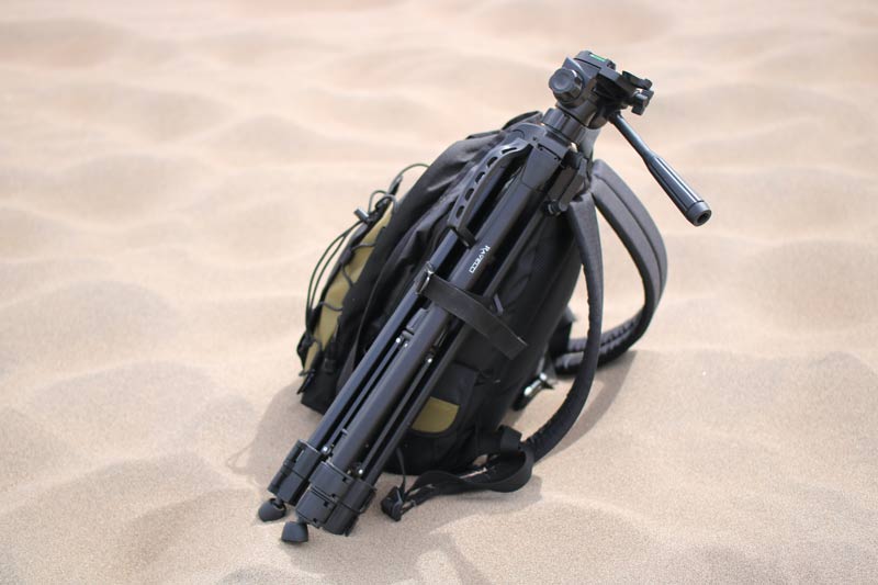 Camera backpack with a tripod strapped to it during a sea photography shoot