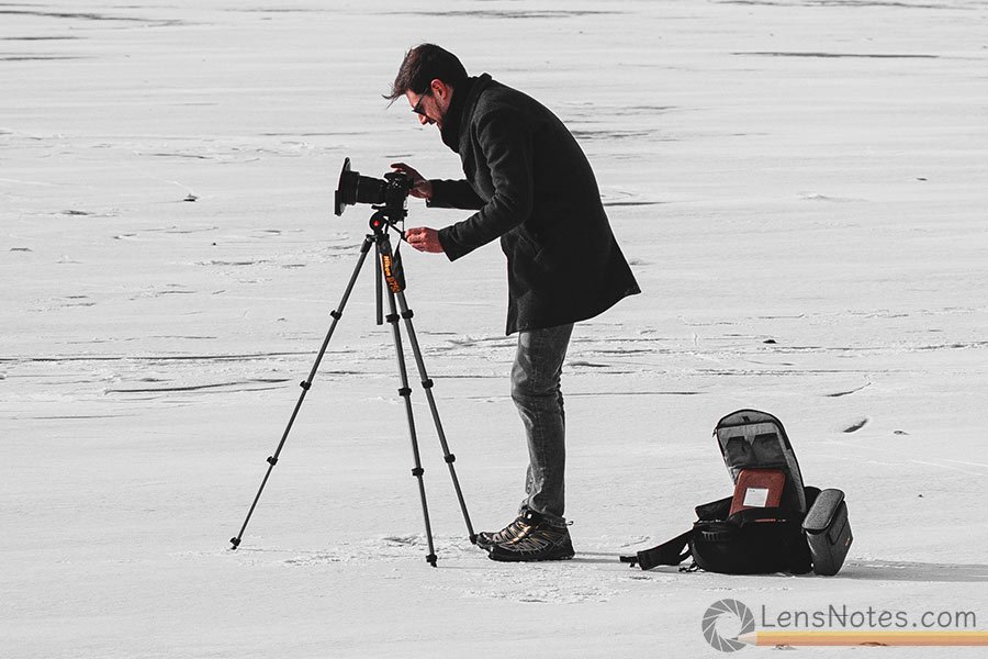 Photographer with a camera on a tripod shooting  on a frozen lake